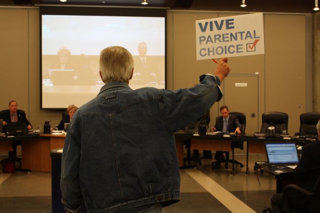 Retired teacher Chris Eustace holds up a sign calling for more parental choice in language of schooling for their children. Eustace said Pearson's resolution calling for the same thing is too 'watered-down.'  photo : Sarah Leavitt